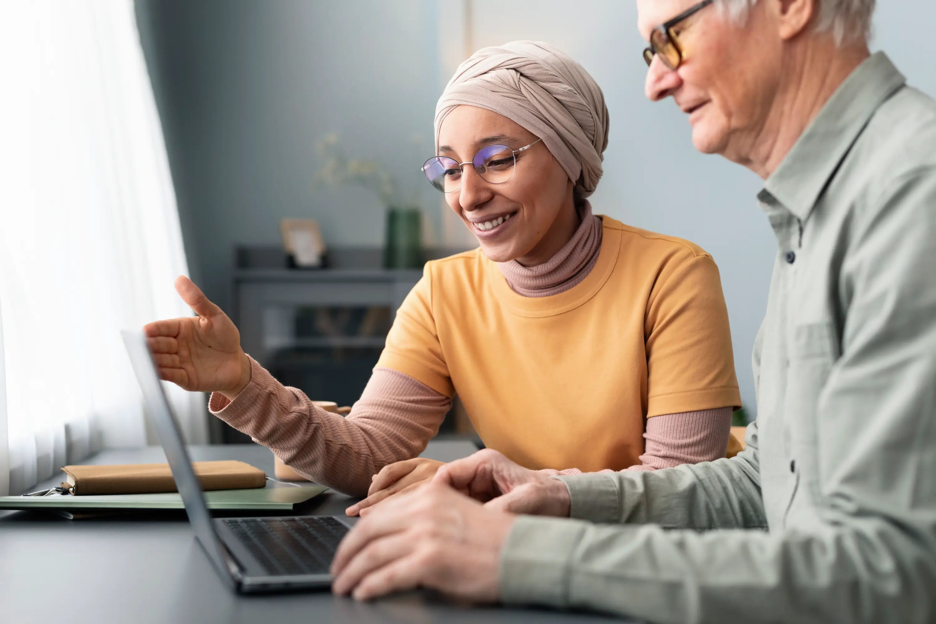 Two elderly individuals, one wearing a headscarf, using a laptop together.