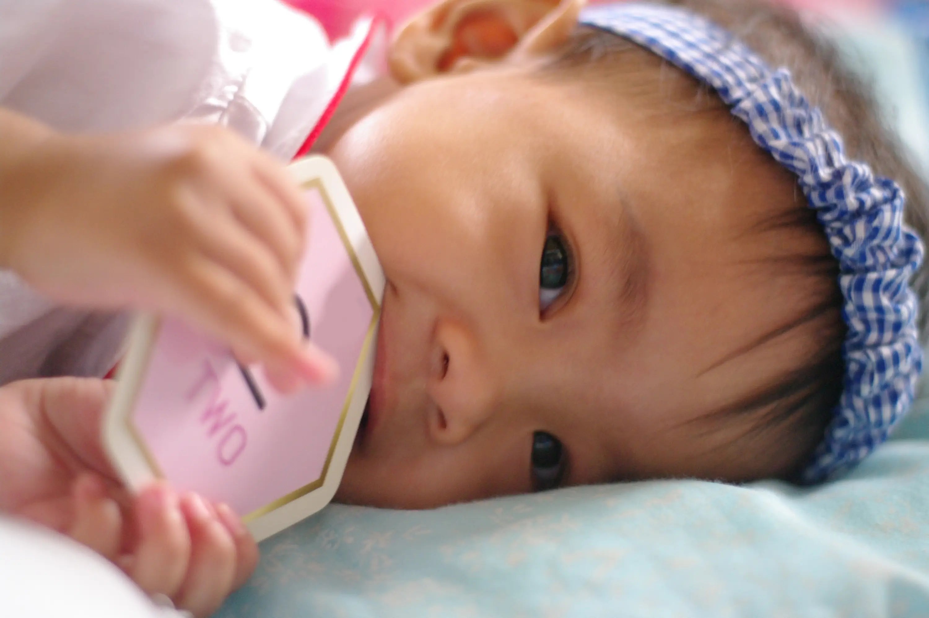Bébé allongé sur une couverture rose avec un bandeau bleu, jouant avec un jouet rose.