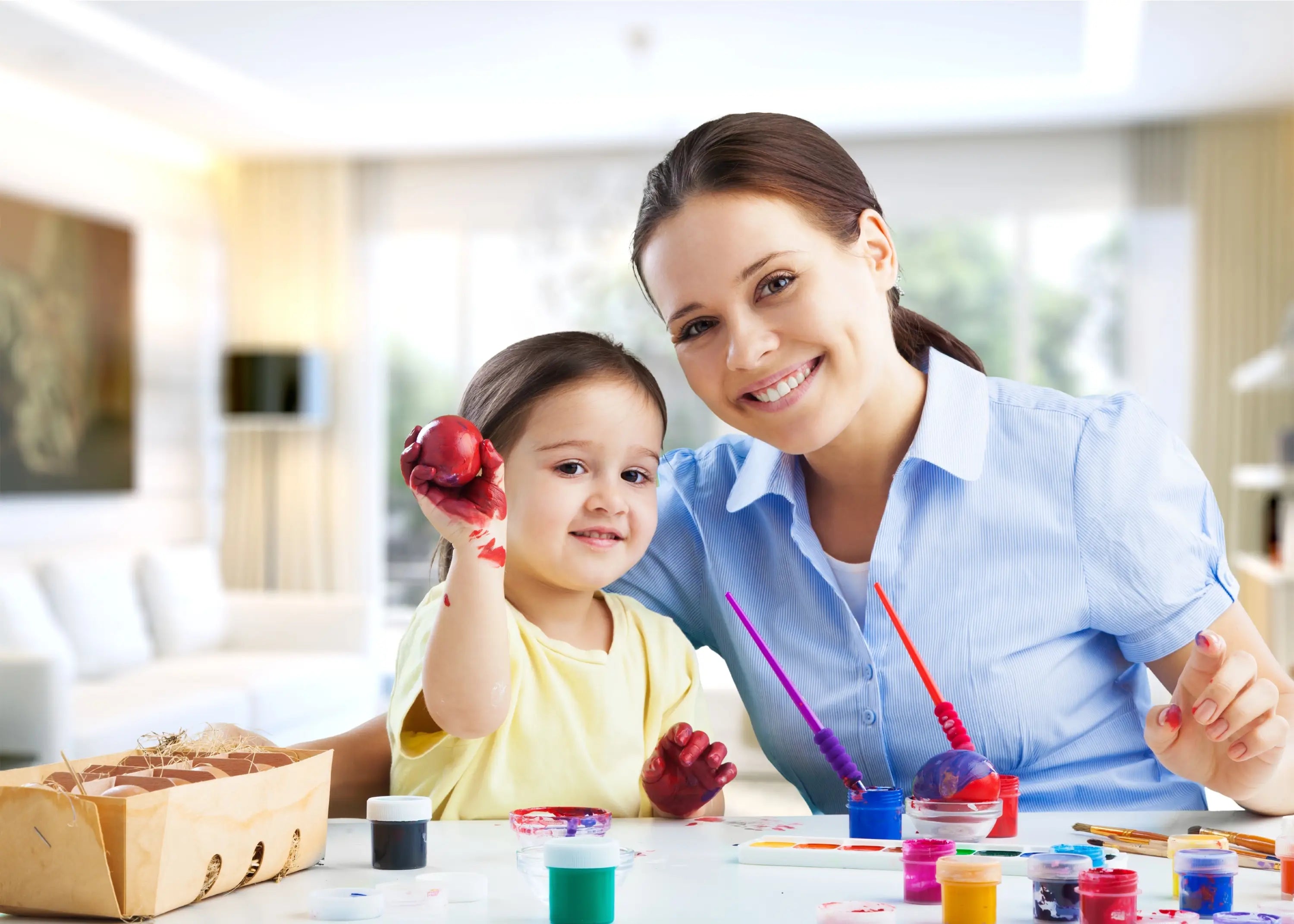Woman and child engaged in an art activity with paint and brushes.