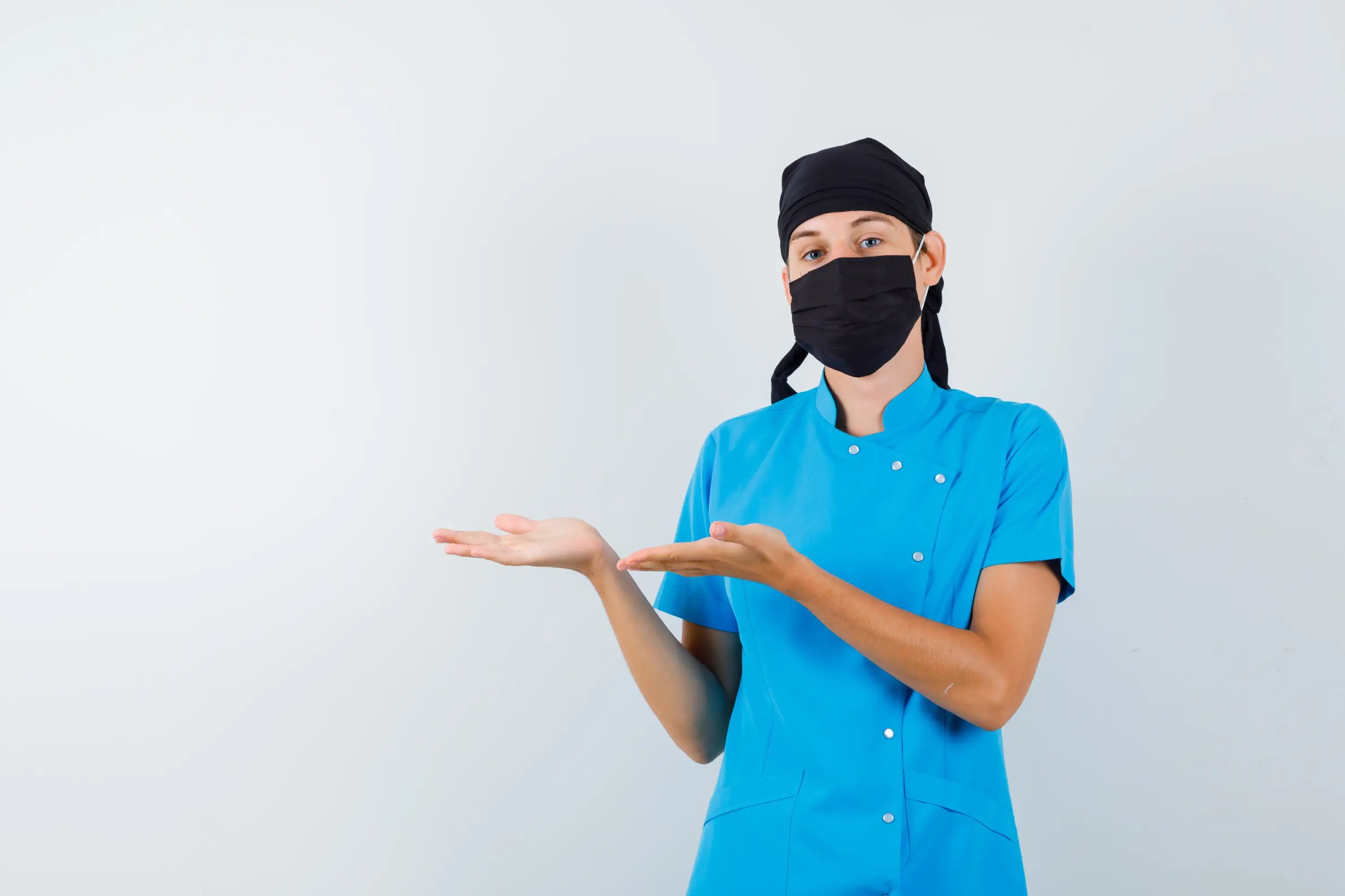 Person in blue medical scrubs with a black face mask and cap on a white background