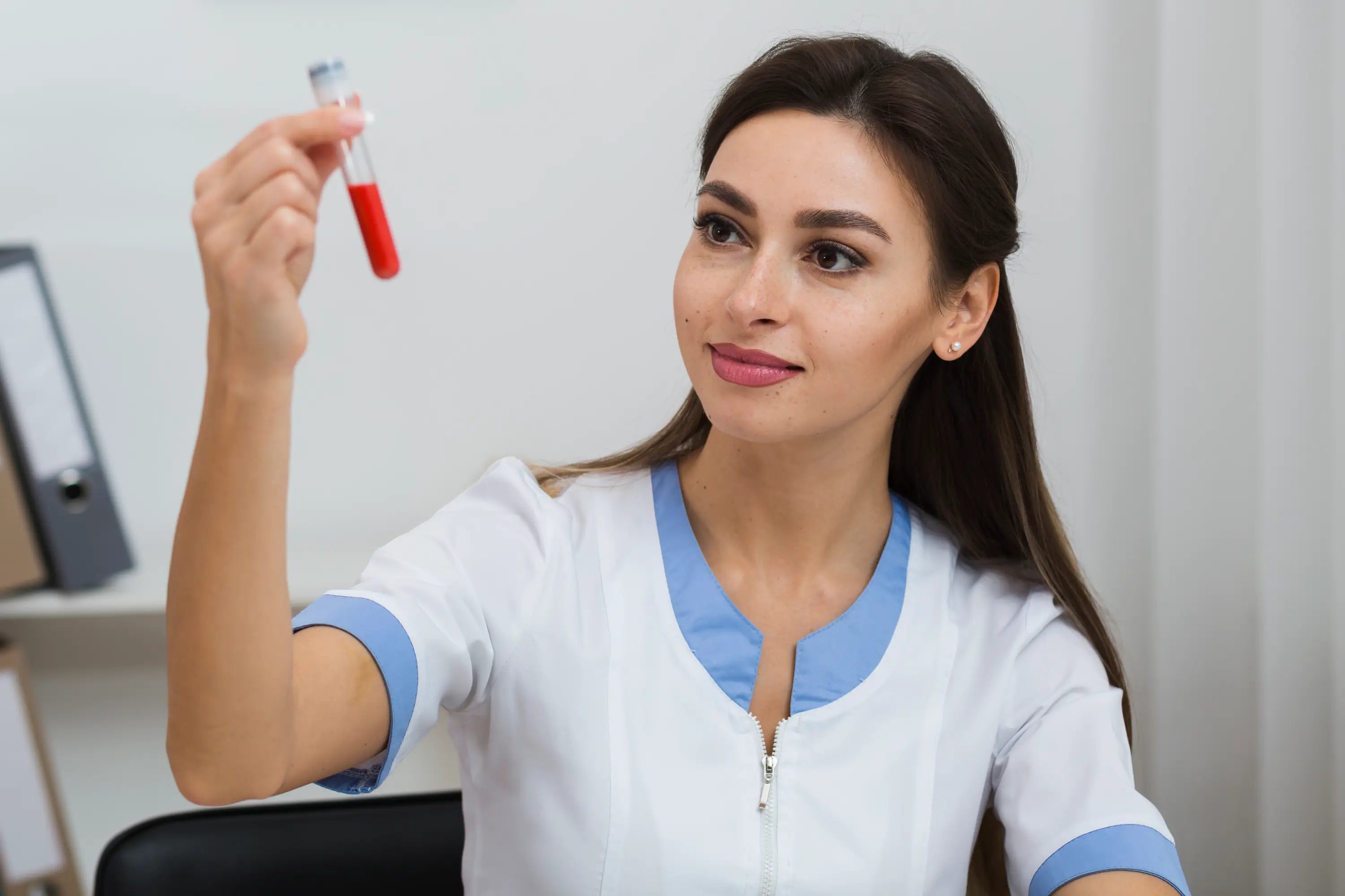 Woman in a medical uniform holding a test tube with red liquid against a white background