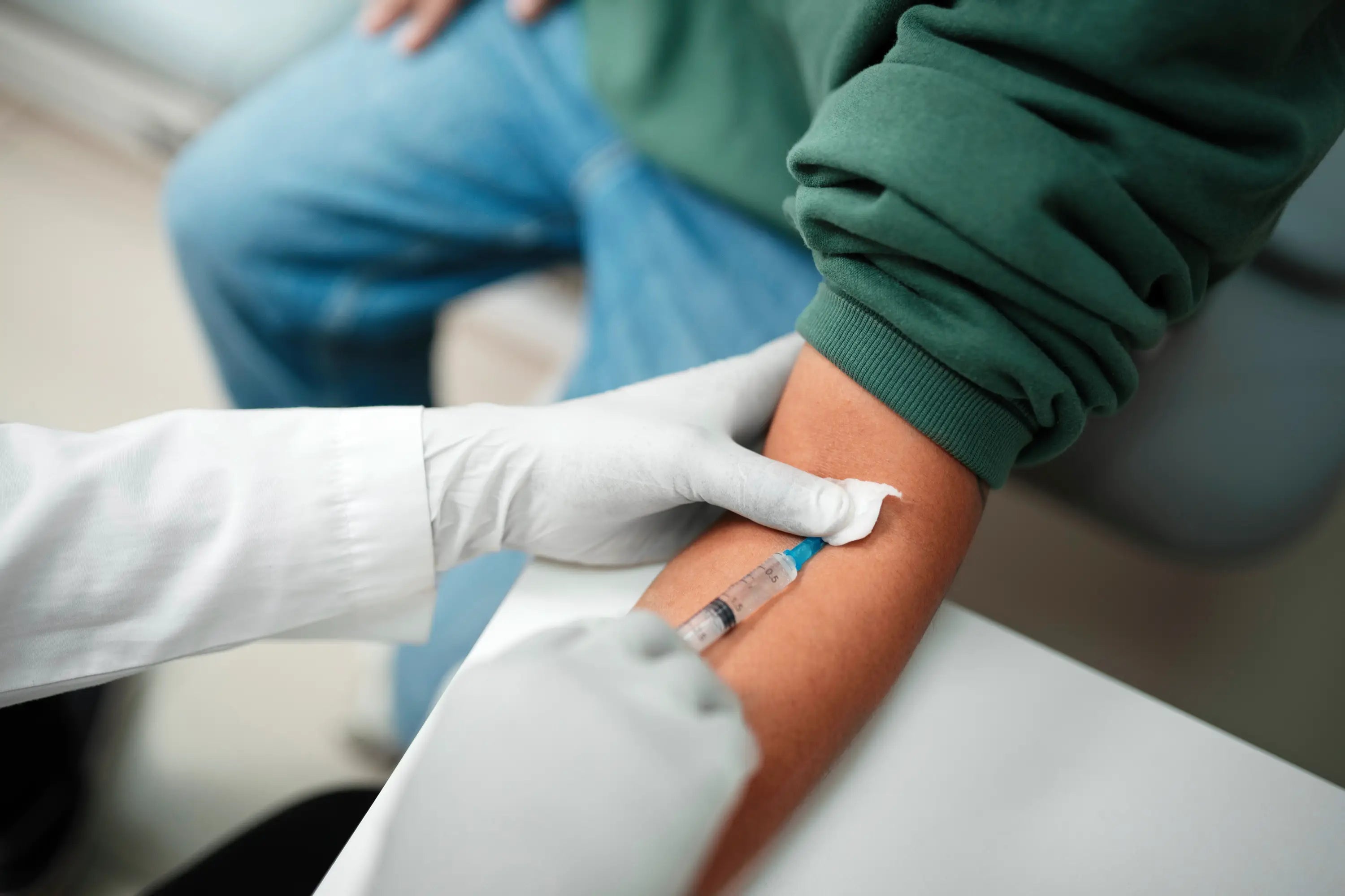 Person receiving a blood sample from a healthcare professional wearing gloves.