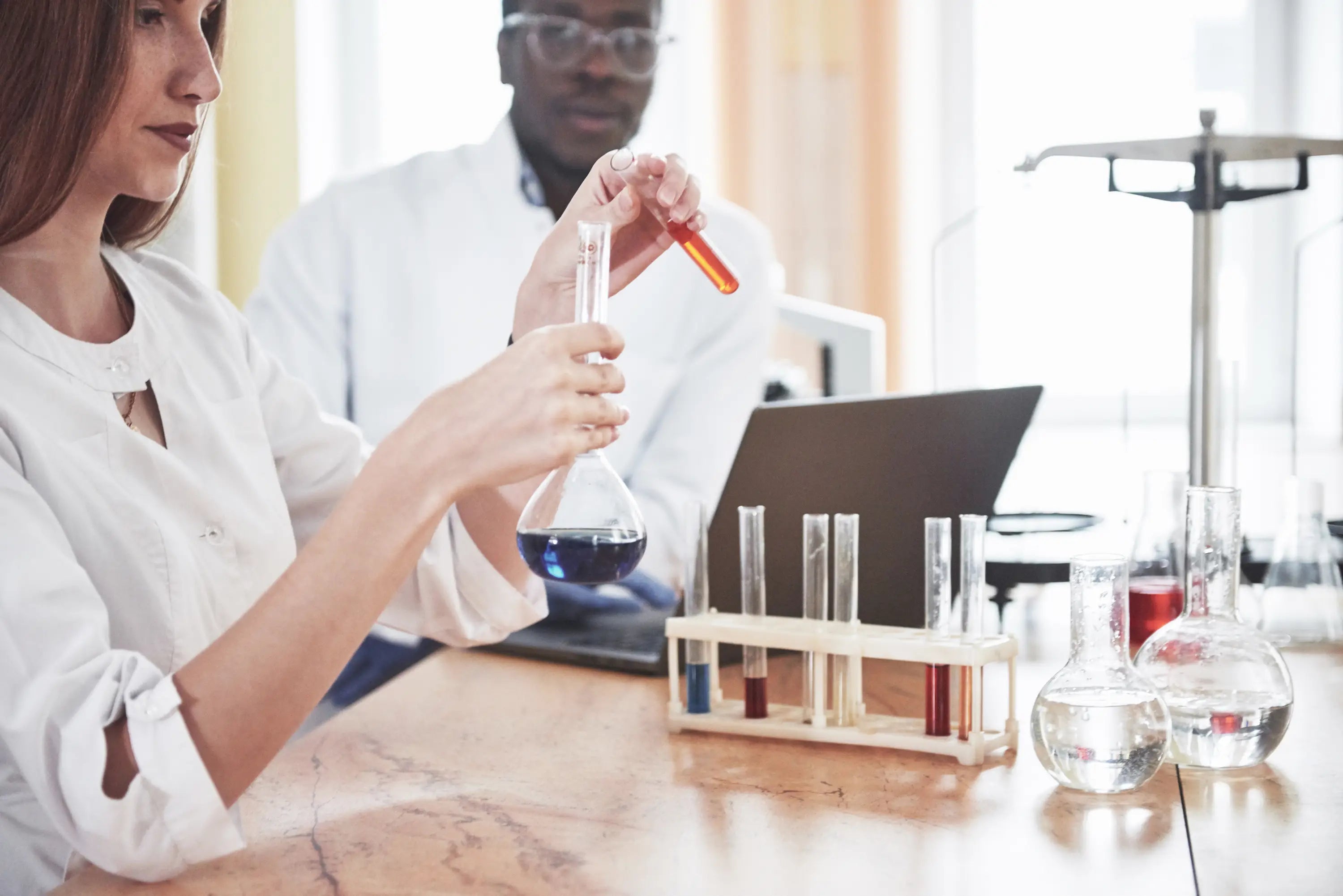 Two scientists working in a laboratory with test tubes and a laptop.