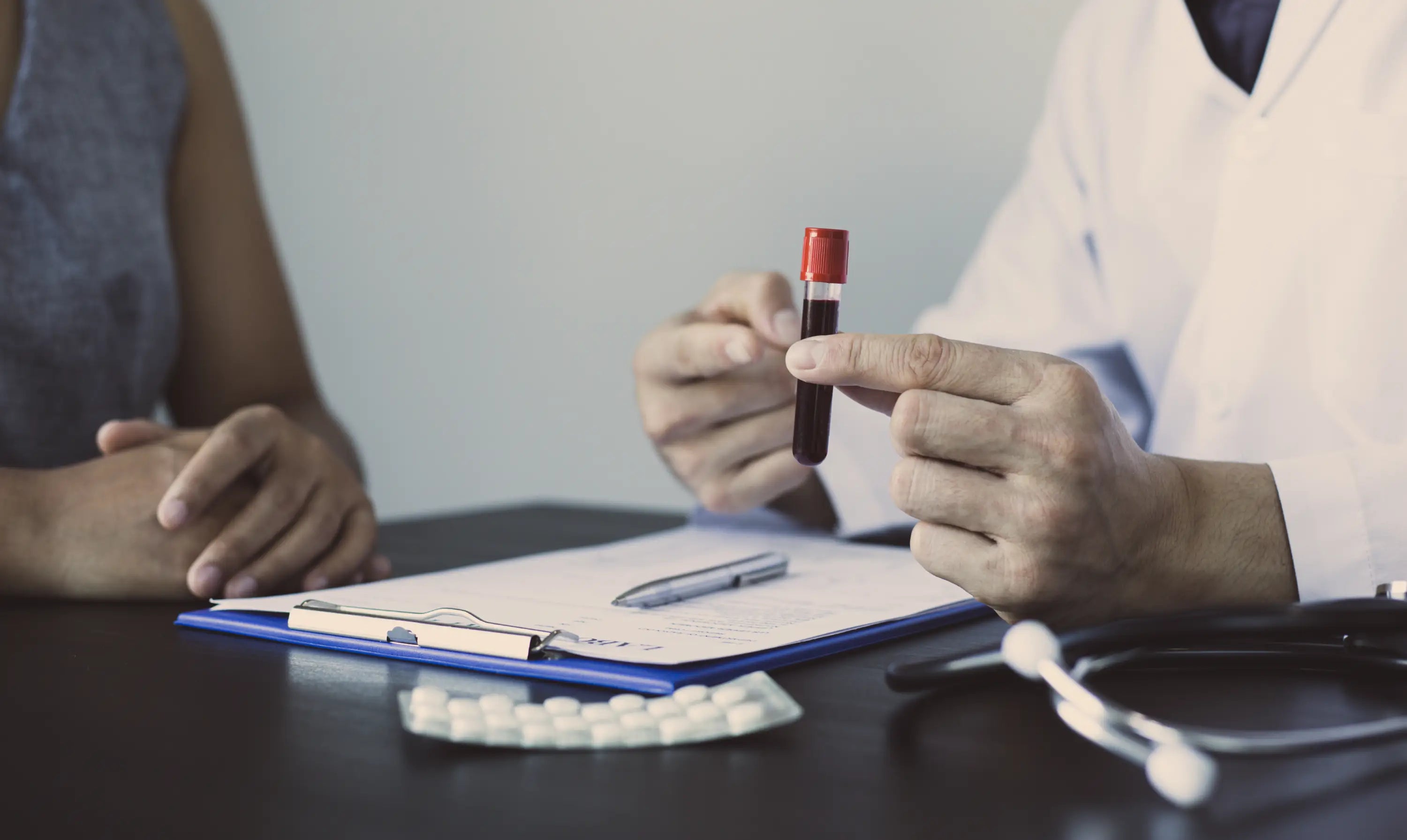 Doctor holding a blood sample tube with a patient and medical records on a table.