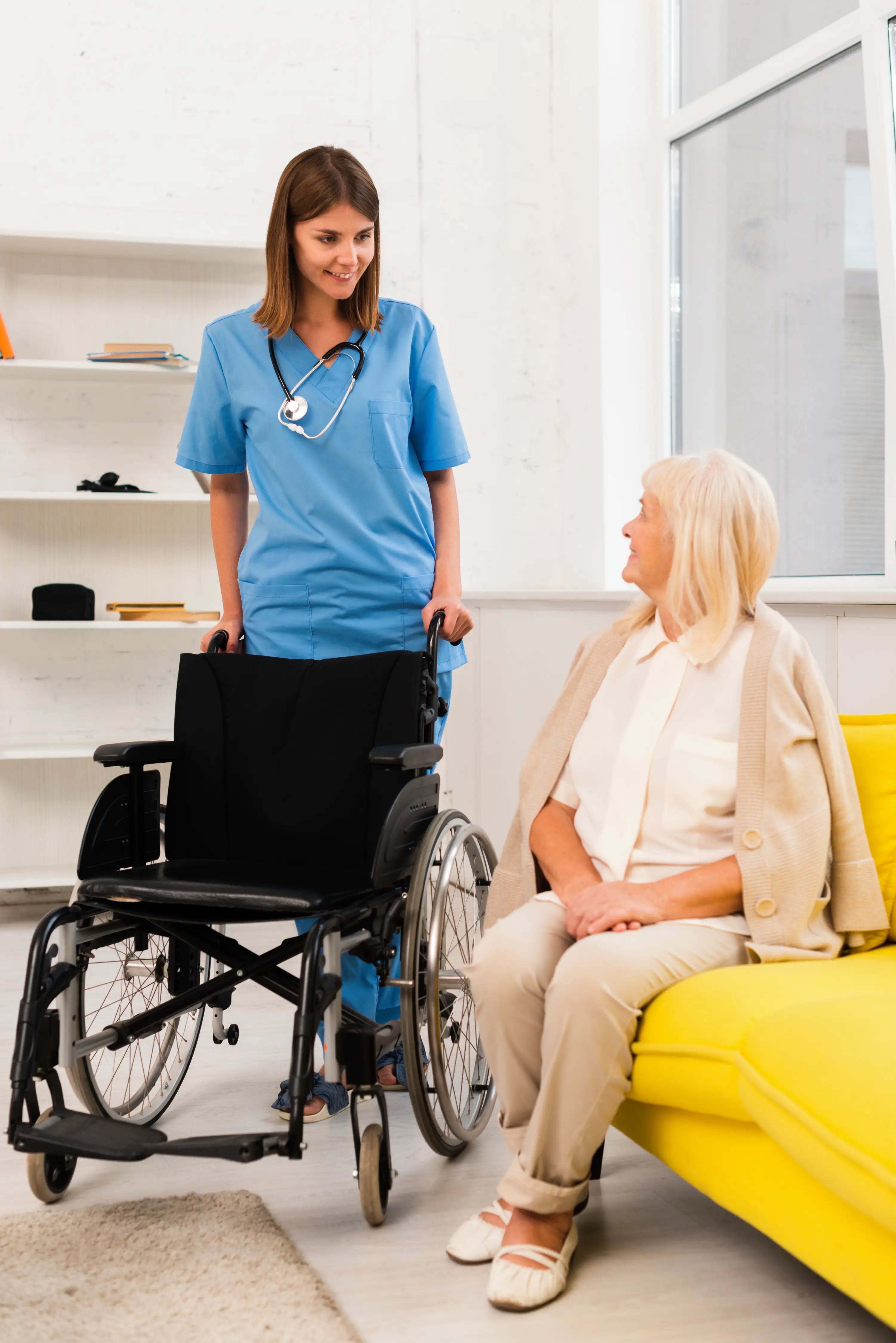 Nurse with a wheelchair talking to a patient in a bright room.