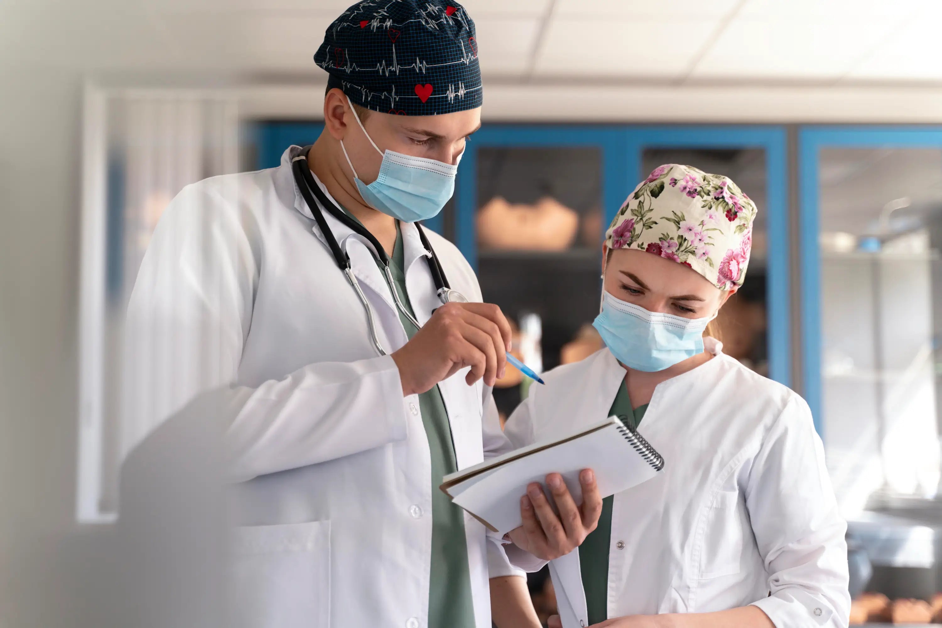 Two healthcare professionals in a hospital setting, one writing on a clipboard.