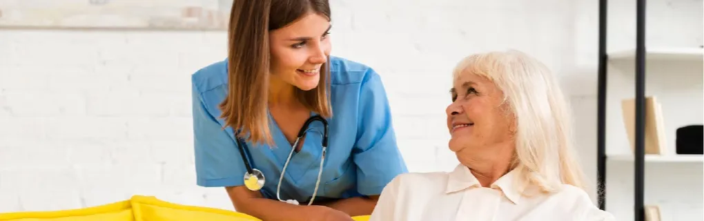 A nurse in a blue uniform smiling at an elderly woman during a general health checkup.