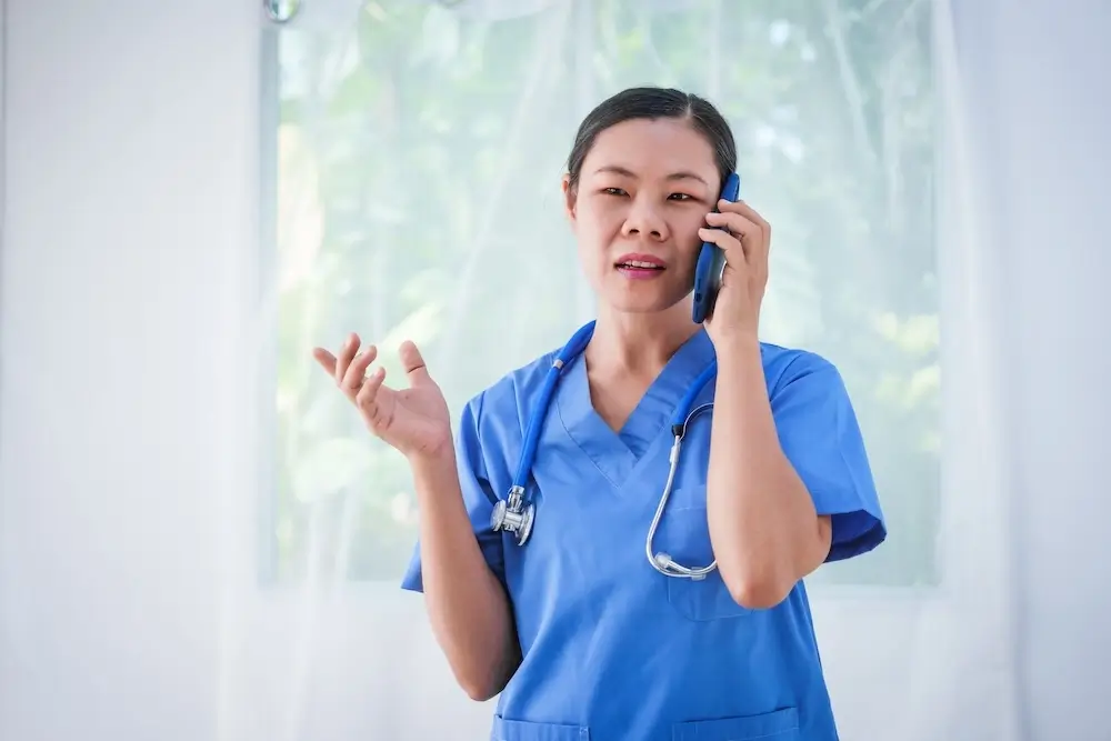 filipina female nurse in blue scrubs speaking on the phone, providing professional healthcare assistance