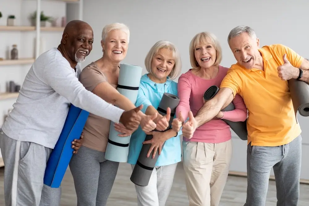 Group of active seniors with yoga mats giving thumbs-up, representing healthy and active lifestyles supported by Clear Diamond Care in Qatar