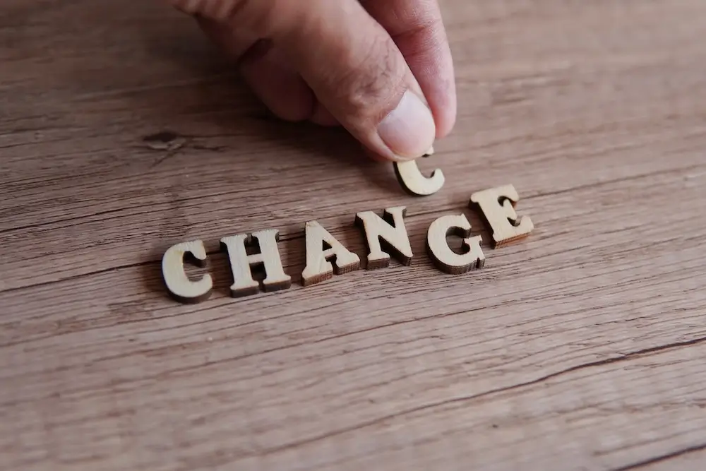 Hand adjusting wooden letters to change the word 'CHANGE' into 'CHANCE' on a wooden surface