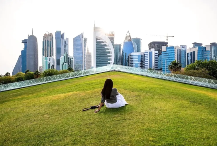 Woman sitting on a green lawn overlooking the modern skyline of Doha, Qatar.