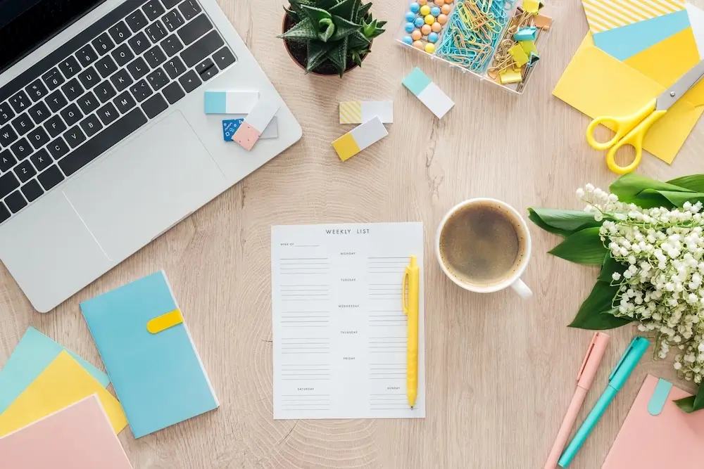 Flat lay of a workspace with a laptop, weekly planner, coffee cup, and colorful stationery items